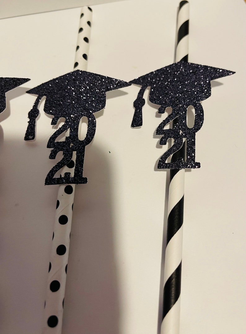 Puede incluir: Pajitas rayadas en blanco y negro y con lunares con gorros de graduaci&oacute;n de purpurina negra y el a&ntilde;o 2021 adjunto.