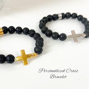 May include: Two personalised cross bracelets. One has a gold cross with "James" engraved, the other a silver cross with "John". Both bracelets feature black lava stone beads. The text "Personalised Cross Bracelet" is also visible.