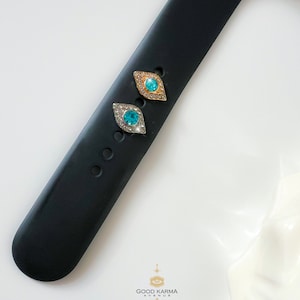 May include: Two small, diamond-shaped charms with an evil eye design. The charms are gold and silver with blue and turquoise rhinestones.