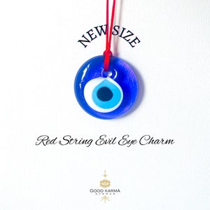 Puede incluir: Amuleto de ojo turco azul en una cuerda roja. El amuleto es redondo y tiene un centro blanco con un ojo azul. El texto "NEW SIZE" está por encima del amuleto.