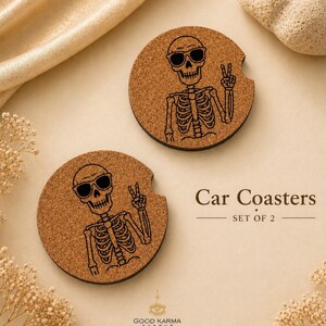 May include: Two round car coasters made of cork, each featuring a black skeleton wearing sunglasses and giving a peace sign. The text "Car Coasters SET OF 2" is printed in black.