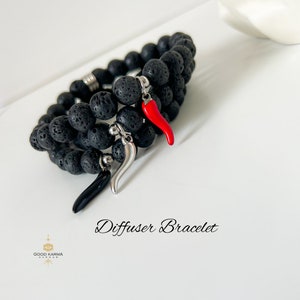 May include: A black lava stone diffuser bracelet with two red and one black chili pepper charms. The bracelet is layered and has a silver clasp. "Diffuser Bracelet" is written in cursive below the bracelet.