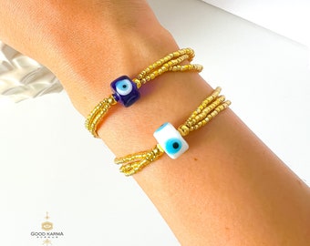 May include: Two gold beaded bracelets with evil eye charms. One charm is blue and white, the other is white and blue.
