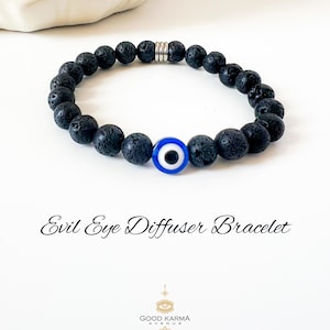 Può includere: Braccialetto con perline in pietra lavica nera con un ciondolo a forma di occhio blu e bianco. Il braccialetto è infilato su un cordino elastico. Il testo "Evil Eye Diffuser Bracelet" è visibile.