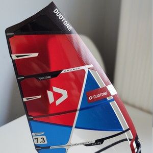 Puede incluir: Una vela de windsurf roja, blanca y azul con el logotipo de Duotone y el texto "7.3 E-Type".