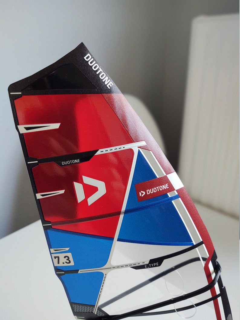 Puede incluir: Una vela de windsurf roja, blanca y azul con el logotipo de Duotone y el texto "7.3 E-Type".