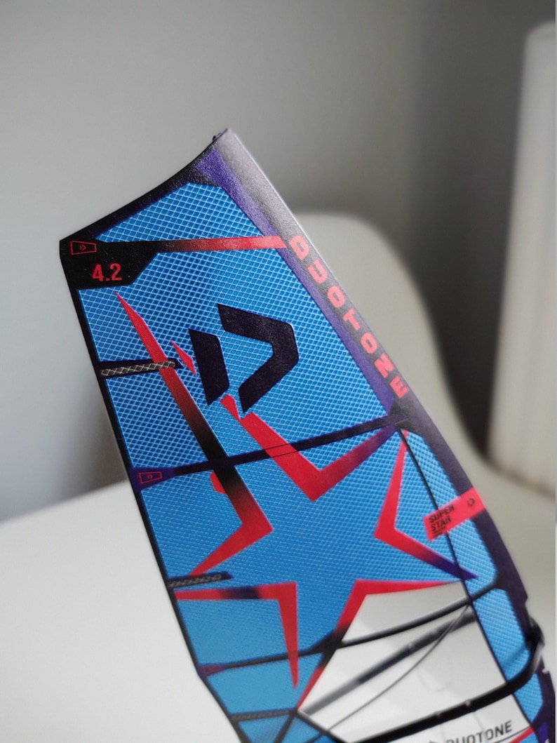 May include: A blue and red windsurf sail with a white star and the text "DUOTONE" and "SUPER STAR" printed on it. The sail is numbered "4.2".