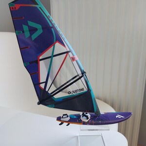 May include: A miniature windsurfing setup featuring a purple and teal sail with the text "DUOTONE" and a matching purple board. The sail has a blue and red design with the number "4.2". The board has black fins.
