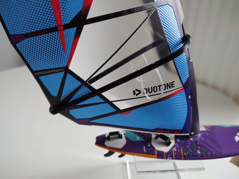 May include: A blue and black windsurf sail with a red stripe and a white logo that says "DUOTONE".