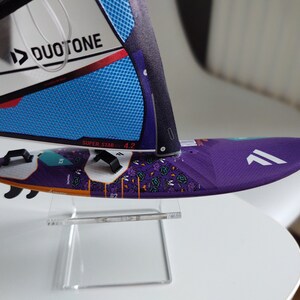 May include: A purple and white windsurf sail with a black and blue DUOTONE logo and the text "SUPER STAR 4.2" on the sail. The sail is on a clear acrylic stand.