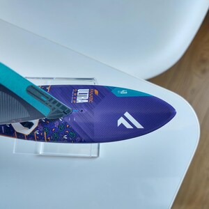 May include: A blue and purple windsurf board with the word "ULTRA" printed on it. The board has a white logo and the number "40" printed on it. The board is on a clear stand.