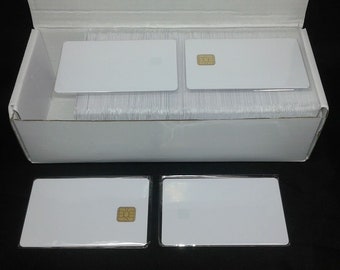 May include: A collection of white plastic cards, some with embedded gold-colored chips, are displayed in a white cardboard box. Several cards are stacked inside the box, while others are arranged outside. The cards have a rectangular shape.