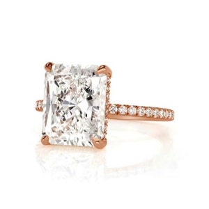 May include: A rose gold engagement ring with a large, square-shaped diamond center stone and a band of smaller diamonds.