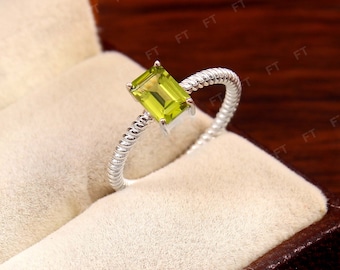 May include: A silver ring with a twisted band and a green gemstone in an emerald cut.