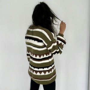 May include: A green, white, and brown striped sweater with a geometric pattern. The sweater has long sleeves and a relaxed fit.