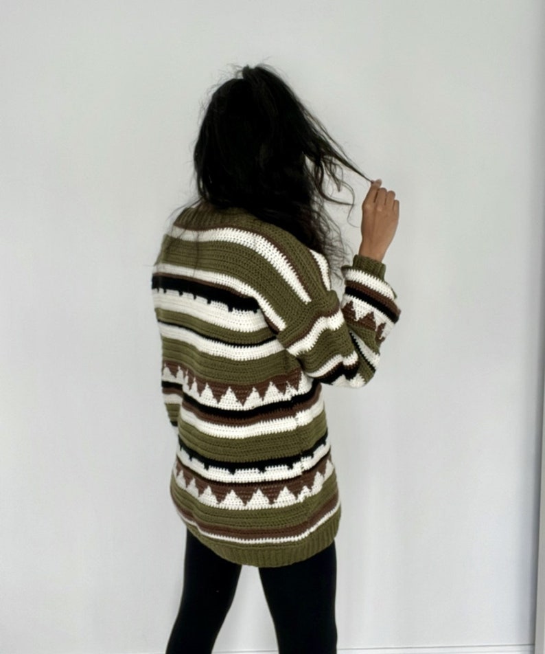 May include: A green, white, and brown striped sweater with a geometric pattern. The sweater has long sleeves and a relaxed fit.