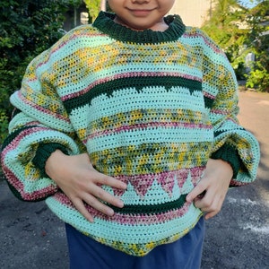 May include: A green, pink, and yellow striped crocheted sweater with a green and pink trim. The sweater has a loose fit and a round neckline.