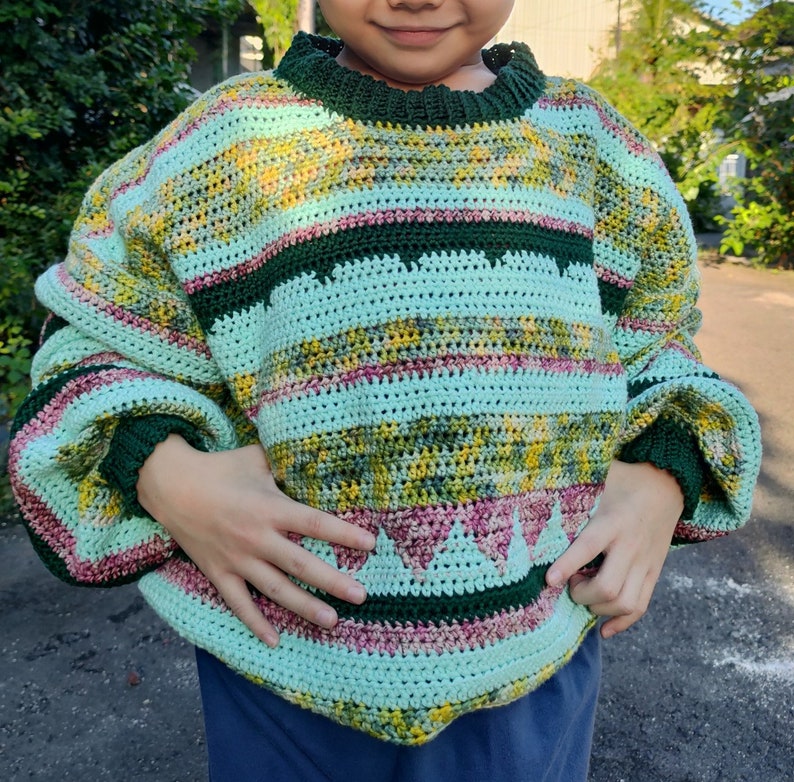 May include: A green, pink, and yellow striped crocheted sweater with a green and pink trim. The sweater has a loose fit and a round neckline.
