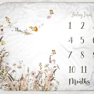 Könnte beinhalten: Eine weiße Baby-Meilenstein-Decke mit floralem Design und dem Text "Today I am..." gefolgt von den Zahlen 1 bis 12 und dem Wort "Months".