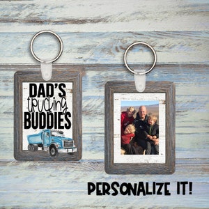 Puede incluir: Dos llaveros de fotos de madera con fondo blanco y marco de madera desgastado. Un llavero presenta un camión azul con el texto "Dad's trucking buddies". El otro llavero presenta una foto de una familia de cuatro.