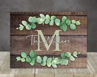 May include: A rustic wooden sign with a green eucalyptus wreath and the text "The Millers" with a large letter "M" in the center.