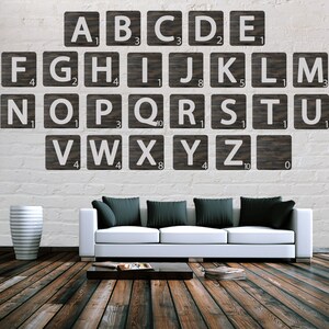 Pode incluir: Um sofá branco com almofadas pretas fica em frente a uma parede de tijolo branco com peças de Scrabble de madeira que soletram o alfabeto. Cada peça tem um número.