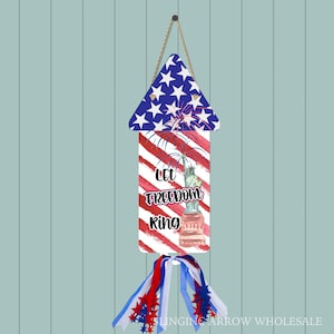 May include: A red, white, and blue firework-shaped door hanger with the Statue of Liberty and the text "Let Freedom Ring".