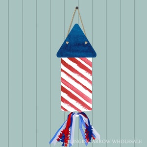 May include: A red, white, and blue firework decoration with a blue triangle top and red and white striped body. The decoration is hanging from a string and has a blue, white, and red ribbon tail with stars.