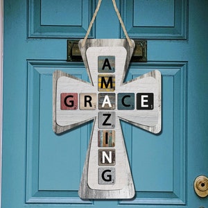 以下が含まれることがあります： カラフルなスクラブルタイルを使って「AMAZING」という単語を綴った木製十字架。十字架は青いドアに掛けられています。