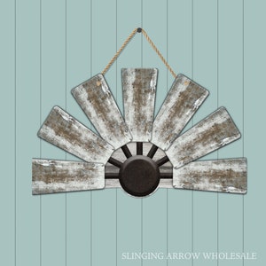 May include: A rustic windmill wall decor with weathered white and brown blades, a black center, and a natural rope hanger. The windmill is mounted on a light blue, vertical-slat background. The text "SLINGING ARROW WHOLESALE" is at the bottom.