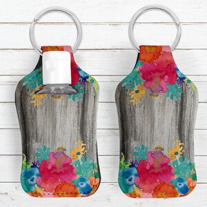 May include: Two gray and white hand sanitizer holders with a floral design. The holders have a key ring and are made of fabric. The floral design features red, orange, yellow, blue, and green flowers.