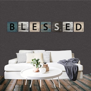 Puede incluir: Un sofá blanco con almohadas y una manta se encuentra frente a una pared gris con la palabra "BLESSED" escrita en letras negras sobre azulejos de madera.
