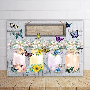 May include: Three mason jars with floral arrangements and butterflies, painted in a watercolor style. The jars are decorated with polka dots, stripes, and flowers. A wooden sign with a burlap background hangs above the jars.