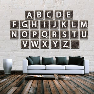 Könnte beinhalten: Eine weiße Wand mit einem Satz Alphabet-Kacheln, die in Reihen angeordnet sind. Jede Kachel ist aus Holz und hat einen Buchstaben und eine Zahl darauf. Die Kacheln sind in alphabetischer Reihenfolge angeordnet. Ein weißes Sofa mit schwarzen Kissen steht vor der Wand.