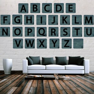 Pode incluir: Um sofá branco com almofadas pretas fica em frente a uma parede de tijolo branco com azulejos de alfabeto azul e branco. Os azulejos estão dispostos em ordem alfabética e cada azulejo tem um número.