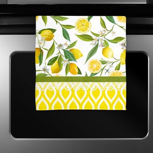 Op de afbeelding: Een witte keukendoek met een citroenprint. De handdoek heeft een groene en witte rand en een geel en wit patroon aan de onderkant.