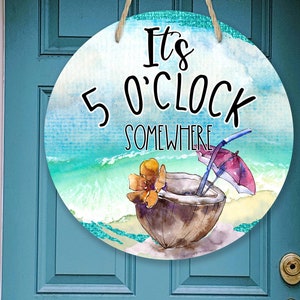 Könnte beinhalten: Rundes Holzschild mit einem Aquarellhintergrund einer Strandszene. Das Schild sagt "It's 5 O'Clock Somewhere" mit einem Kokosnussgetränk und einem Sonnenschirm.