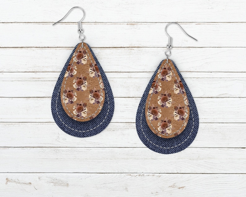 May include: A pair of teardrop-shaped earrings with a brown floral print on the top layer and a dark blue denim layer on the bottom.