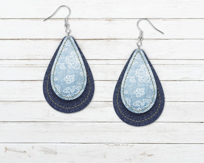 May include: A pair of denim and light blue fabric teardrop-shaped earrings with a white floral pattern.