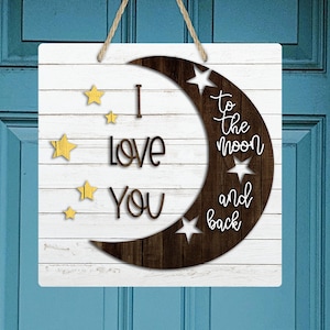 以下が含まれることがあります： 白い背景に茶色の三日月と星が描かれた木製の看板。看板には「あなたを月まで愛してる」と書かれています。