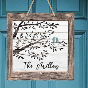 May include: A rustic wooden sign with a white background featuring a silhouette of a tree with two blue birds perched on a branch. The text "The Millers" is written below the tree.