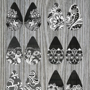 Puede incluir: Nueve pares de pendientes negros y blancos en forma de lágrima con intrincados diseños de encaje. Los pendientes están dispuestos en tres filas de tres.