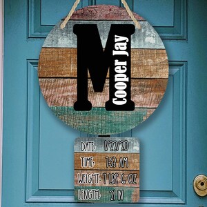 以下が含まれることがあります： 茶色、青、白の色の組み合わせで、木目調の素朴なデザインが施された丸い木製看板。看板には、大きな黒い文字「M」と、黒い文字で「Cooper Jay」という名前が書かれている。その下に、小さな長方形の看板がぶら下がっていて、「DATE: 22/20 TIME 7:53 AM WEIGHT: 7 LBS 6 OZ LENGTH 21 IN」という文字が書かれている。