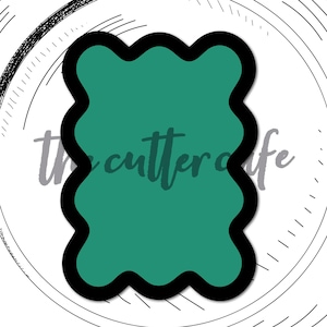 May include: A teal wavy plaque rectangle cookie cutter with a black outline, set against a white plate-like background with sketched details. The text "the cutter cafe" and "wavy plaque rectangle" are visible.