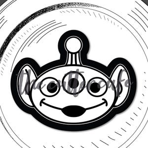 May include: Black and white alien toy design on a white plate with a black border. The alien has three eyes and a smiling mouth. The text "alien toy" is below the plate.