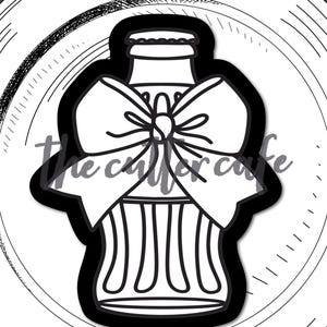 May include: A black and white cookie cutter in the shape of a soda bottle with a bow. The cutter is on a white plate with a black outline. The text "cola bottle w bow" is at the bottom.