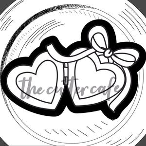 May include: Black and white open locket cookie cutter with two heart shapes, a ribbon, and the text "the cutter cafe". The cutter is on a white plate with the text "open locket" at the bottom.