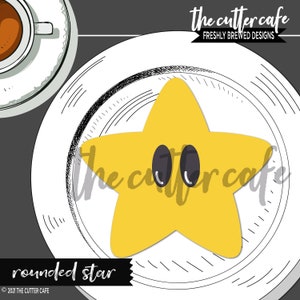 May include: A yellow rounded star cookie cutter with two black circles for eyes. The cutter is on a white plate with a black and white sketched design. The text "the cutter cafe" is written in black on the plate. The text "rounded star" is written in black at the bottom of the image.
