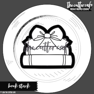 May include: Black and white cookie cutter in the shape of a stack of books topped with a bow. The words "book stack" are at the bottom. The Cutter Cafe logo is at the top right.