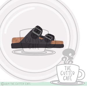 Peut inclure: Une sandale en cuir noir avec deux sangles réglables et un lit de pied marron. La sandale est sur une assiette blanche avec un contour gris. Le texte "The Cutter Cafe" est écrit en noir sur une tasse à café blanche avec de la vapeur qui sort du haut.